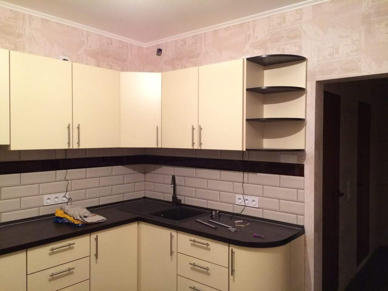 Kuchnia w odcieniach beżu i brązu z czarnym zlewem i białymi kaflami, widoczne akcesoria i narzędzia na blacie.