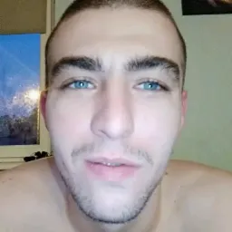 Portret młodego mężczyzny z niebieskimi oczami, widoczny fragment okna w tle.