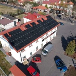 Solar - Ekspert s.c - Widok z lotu ptaka na budynek z panelami słonecznymi na dachu, zaparkowane samochody i chodnik z kostki brukowej.