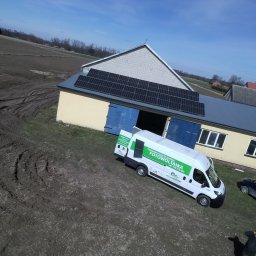 Solar - Ekspert s.c - Instalacja fotowoltaiczna na dachu budynku gospodarczego z zaparkowanym obok samochodem firmowym z logo firmy fotowoltaicznej.