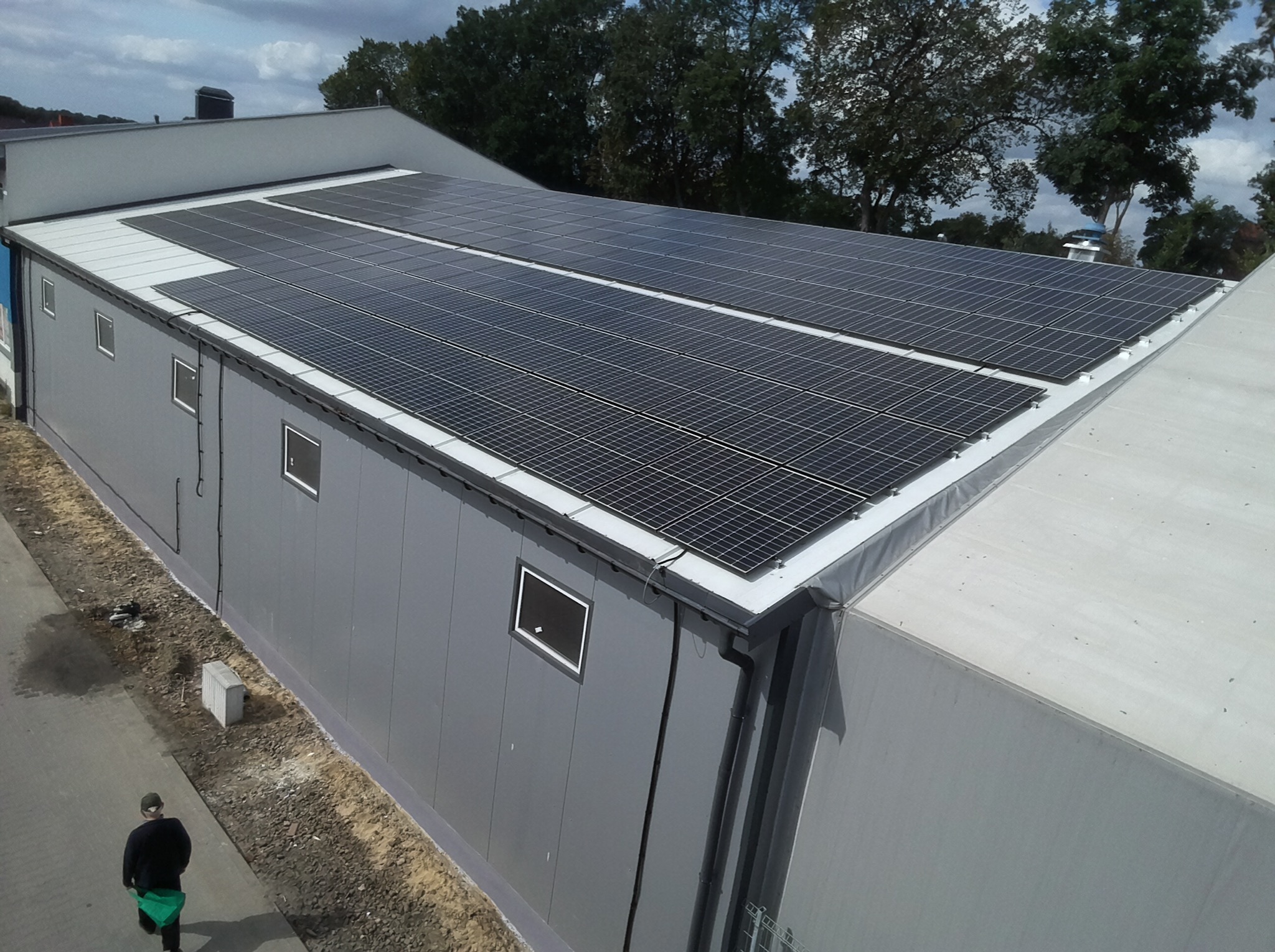 Instalacja fotowoltaiczna na dachu budynku przemysłowego w Nasielsku, widok z góry, osoba przechodząca obok.