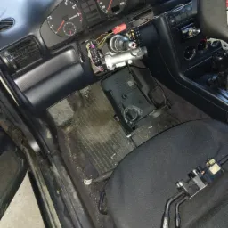 Wnętrze samochodu z rozmontowaną kolumną kierowniczą i elementami deski rozdzielczej, widoczne wskaźniki i przełączniki na fotelu pasażera.