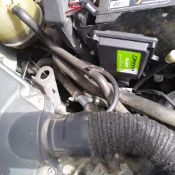 Widok z góry na skomplikowaną instalację w komorze silnika, z widocznym sterownikiem EmmeGas 'READY' 4 CYL, przewodami i elementami układu chłodzenia. W tle akumulator samochodowy.