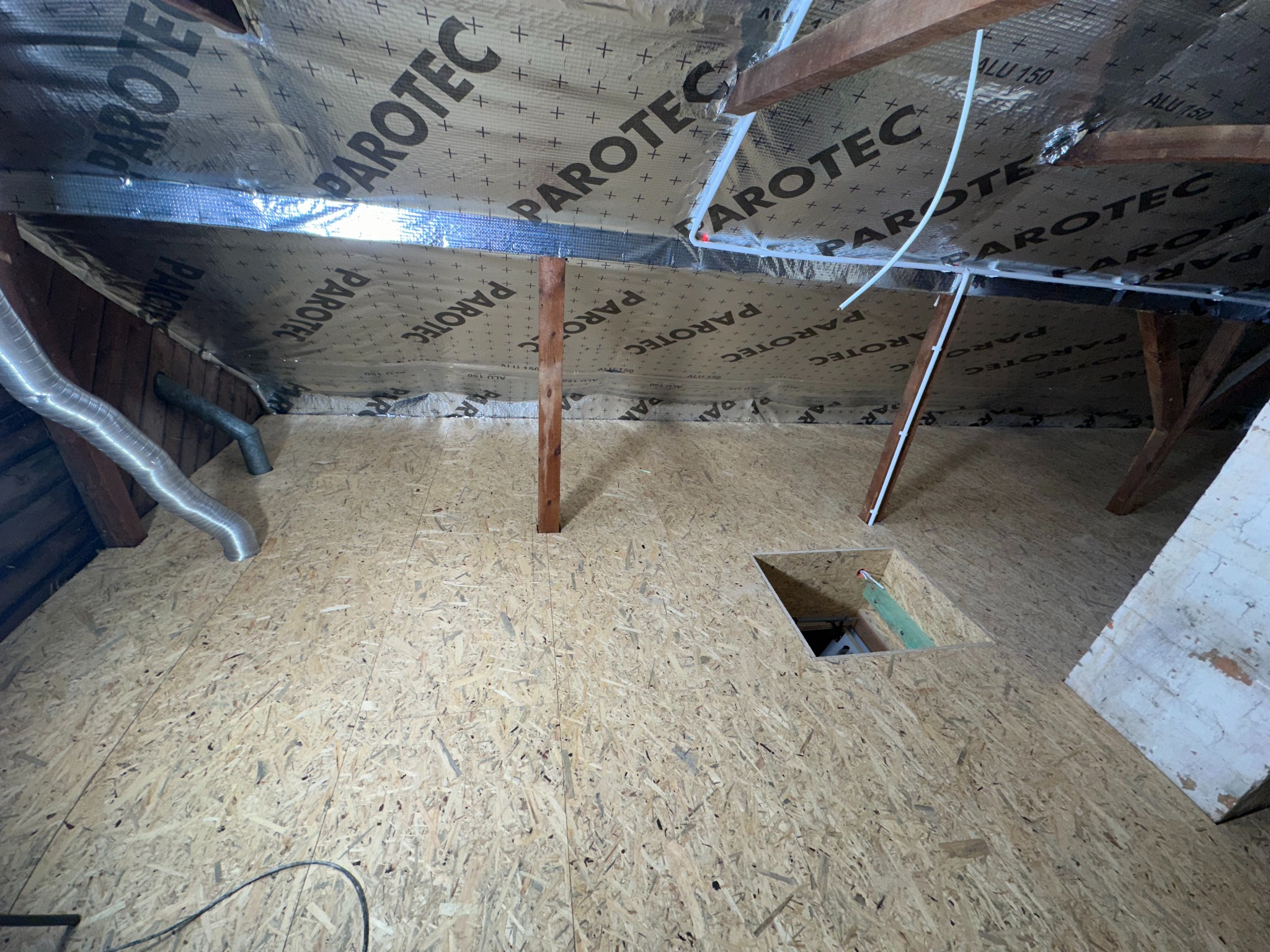 Izolacja poddasza z widoczną folią paroizolacyjną Parotec, drewnianą konstrukcją szkieletową i podłogą z płyty OSB z otworem rewizyjnym.