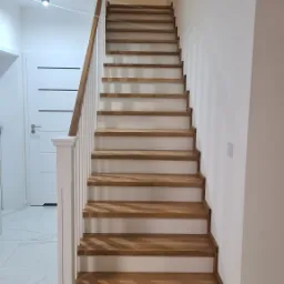 Nowoczesne schody z drewnianymi stopniami i białą balustradą w jasnym wnętrzu, widok z dołu.