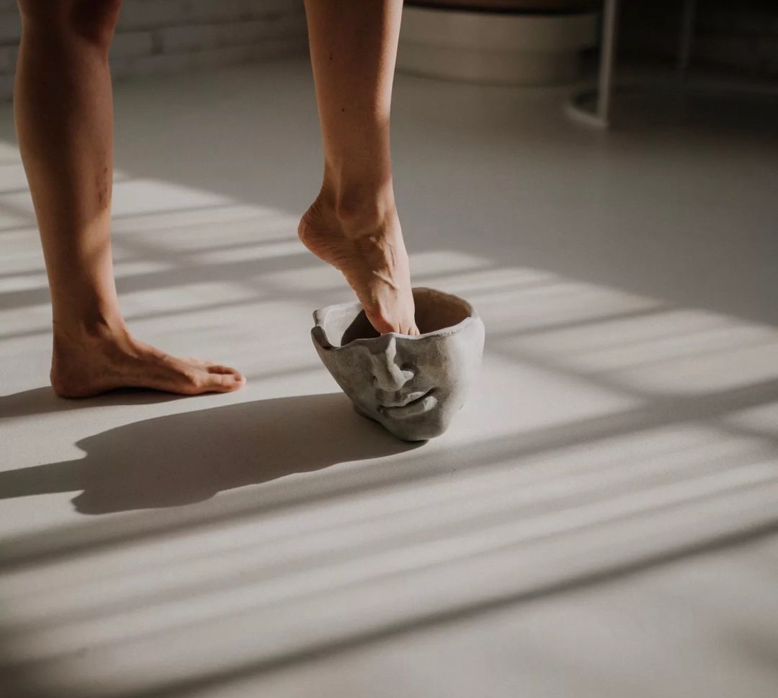 Stopa kobiety w doniczce w kształcie twarzy na jasnej podłodze z cieniami.