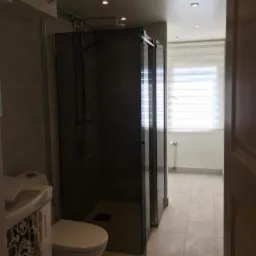 Nowoczesna łazienka z kabiną prysznicową typu walk-in z ciemnego szkła, białą toaletą i umywalką z szafką z wzorzystym frontem.