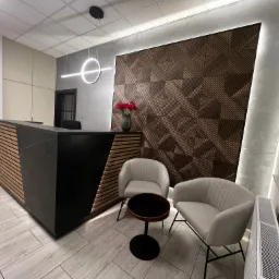 Nowoczesne wnętrze kancelarii: czarna lada recepcyjna z drewnianymi akcentami, geometryczna ściana z paneli, okrągła lampa sufitowa, szare fotele i stolik kawowy, minimalistyczny design.