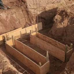 Wykop fundamentów z szalunkiem z płyty OSB i zbrojeniem stalowym, przygotowany do zalania betonem, widok z góry.