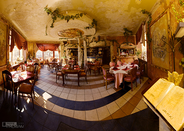 Wnętrze restauracji w stylu rustykalnym z dekoracjami roślinnymi, kolumnami i stolikami nakrytymi do posiłku, widok z szerokiego kąta.