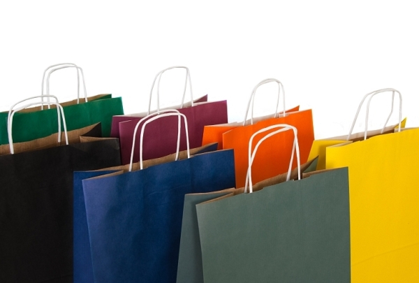 Rząd kolorowych papierowych toreb na zakupy z białymi uchwytami, ustawionych blisko siebie na białym tle.