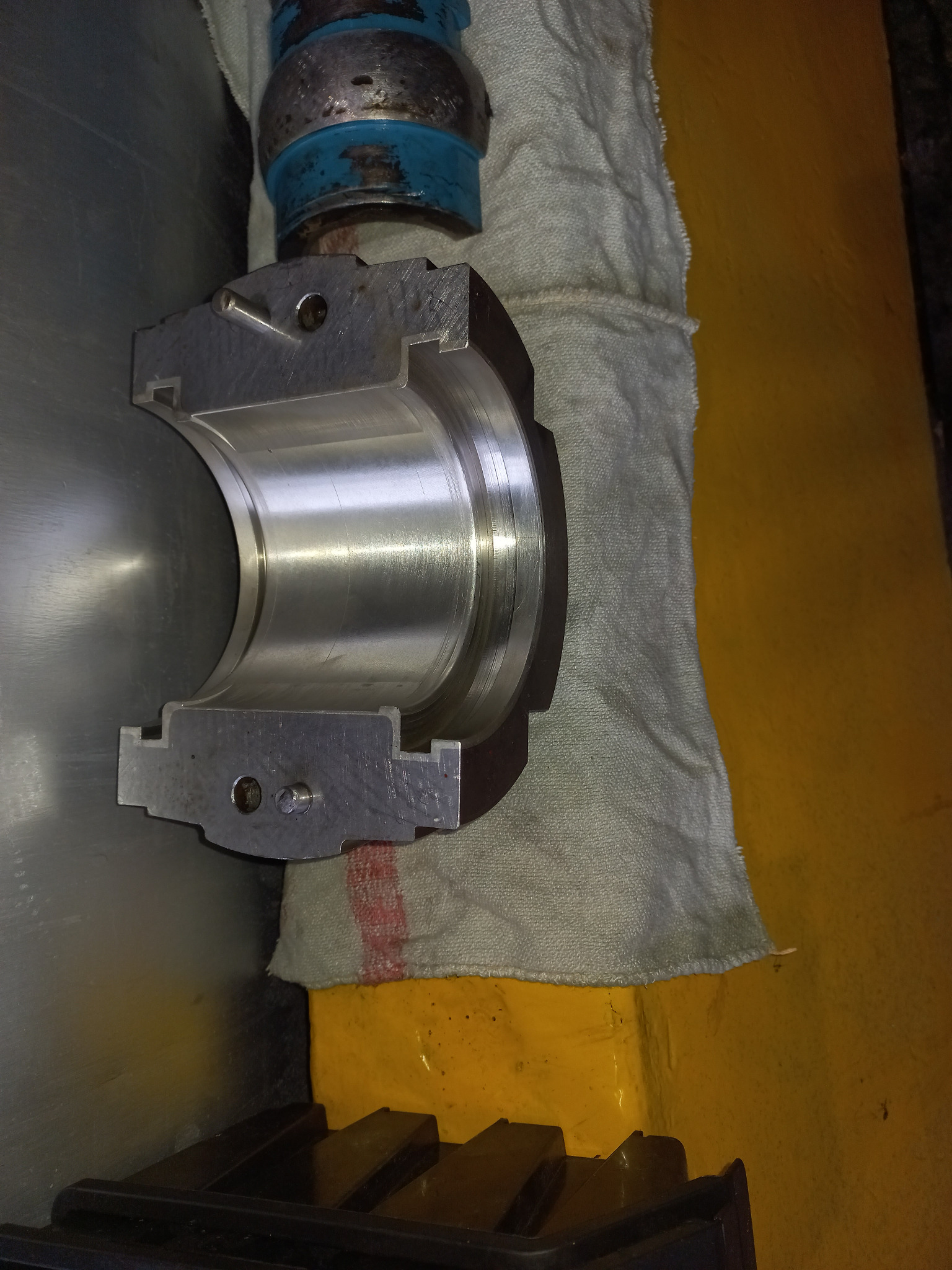 Przekrój poprzeczny precyzyjnie obrobionego, metalowego elementu tulei łożyska, widoczne ślady obróbki skrawaniem, leżący na szarej ściereczce na tle żółtej powierzchni.