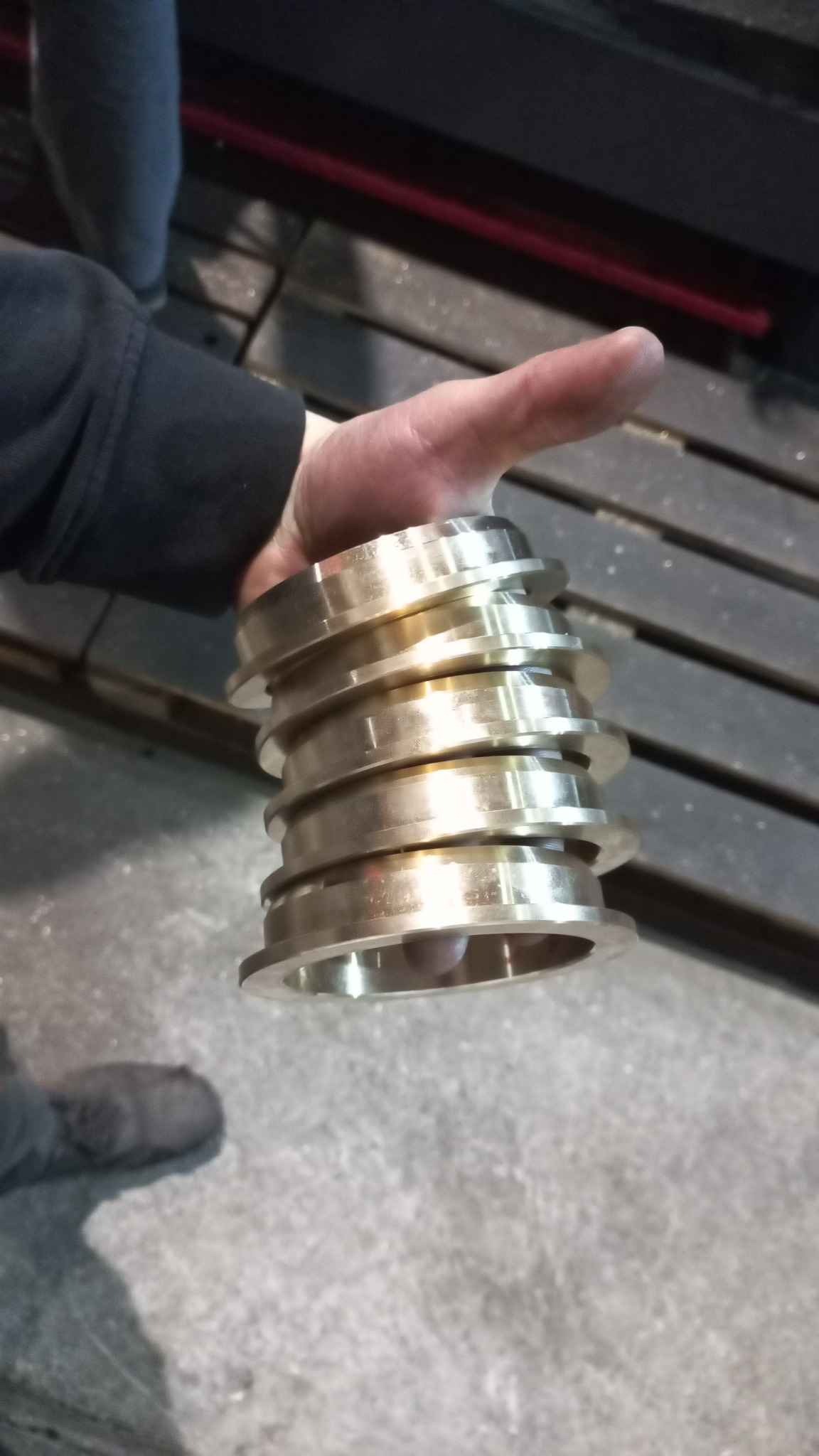 Ręka trzymająca stos obrobionych, metalowych pierścieni z kołnierzami, widoczne ślady obróbki, tło warsztatowe.