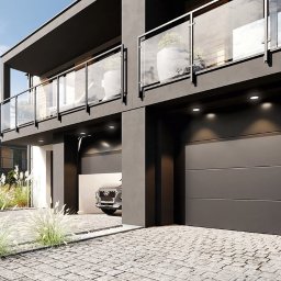 ADAM WOJCIECHOWSKI BRAMYPRO - Nowoczesna, grafitowa brama garażowa segmentowa z oświetleniem punktowym, wkomponowana w architekturę dwukondygnacyjnego domu z balkonami i szklanymi balustradami.