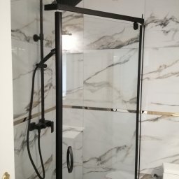 Krzysztof Janas firma ogólnobudowlana - Nowoczesna kabina prysznicowa z czarną armaturą na tle marmurowych płytek w łazience.