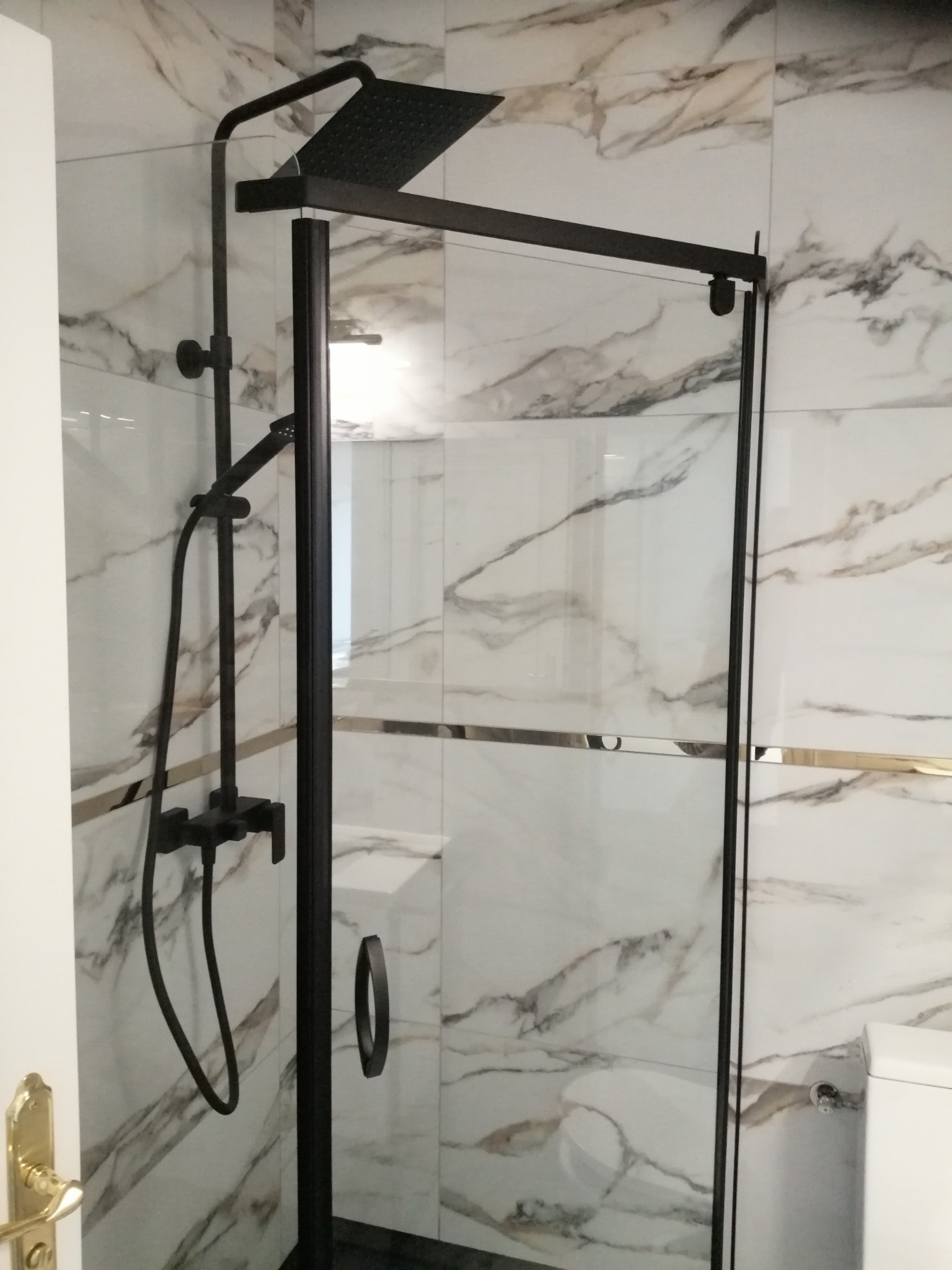 Nowoczesna kabina prysznicowa z czarną armaturą na tle marmurowych płytek w łazience.