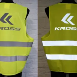 Dwa warianty kolorystyczne kamizelki odblaskowej z nadrukiem 'KROSS' i poziomymi pasami odblaskowymi, prezentowane na manekinie na tle ceglanej ściany.