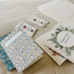 Ręcznie robione kartki okolicznościowe z motywami kwiatowymi i zaproszenia ślubne z zielonymi ornamentami, wizytówki z logo firmy na neutralnym tle.