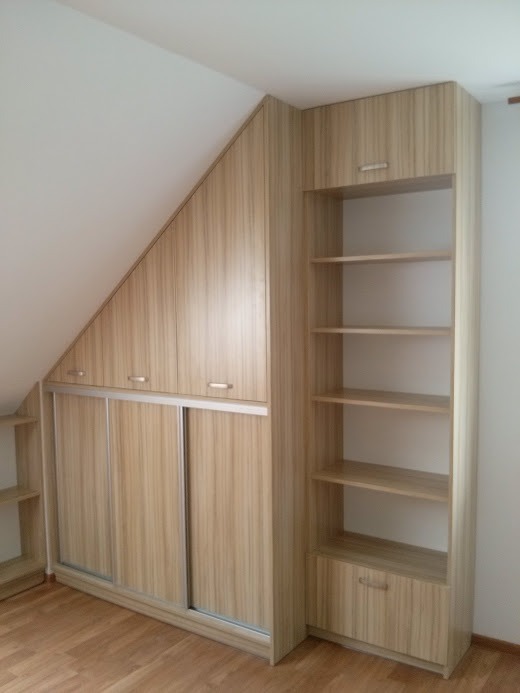 Zabudowa wnęki na poddaszu z przesuwnymi drzwiami i regałem z półkami, wykończona w okleinie drewnopodobnej o jasnym odcieniu.