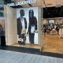 Wystawa sklepowa Karl Lagerfeld z czarno-białą grafiką modela i modelki prezentujących torebki, widoczne półki z produktami i wnętrze sklepu.