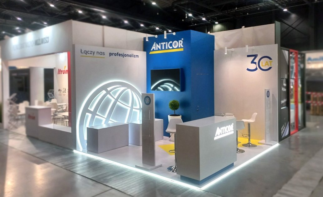 Stoisko targowe firmy Anticor z podświetlanym logo, ekranem i motywem 30-lecia, widoczne krzesła barowe i dekoracyjna roślina.