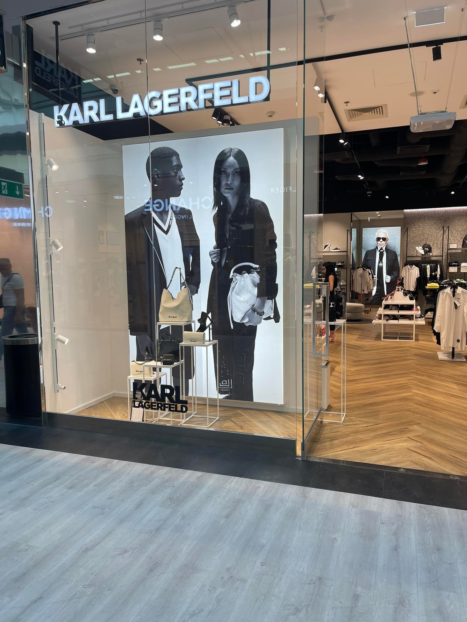 Wystawa sklepowa Karl Lagerfeld z czarno-białą grafiką modela i modelki prezentujących torebki, widoczne półki z produktami i wnętrze sklepu.