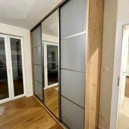 Maiya Harelik Haros.home - Szafa wnękowa z przesuwnymi drzwiami, fronty z lustrami i matowego szkła, obudowa z płyty drewnopodobnej, parkiet na podłodze.