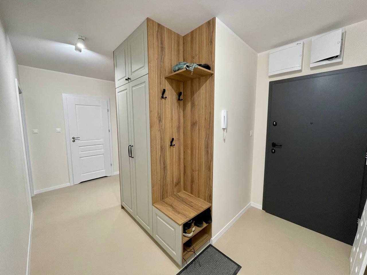 Funkcjonalna zabudowa przedpokoju z szafą, wieszakami i siedziskiem z półkami na buty, utrzymana w kolorystyce drewna i jasnej szarości, dopasowana do niewielkiej przestrzeni.