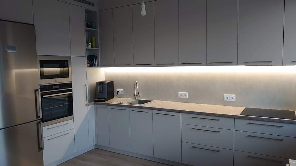 Nowoczesna kuchnia w odcieniach szarości z zabudową na wymiar, oświetleniem podszafkowym LED, sprzętem AGD w zabudowie i ekspressem do kawy na blacie.