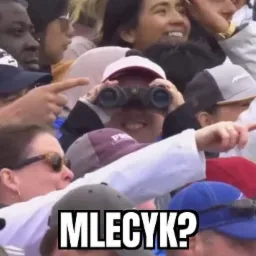 Tłum ludzi, w centrum kobieta z lornetką, a na dole napis 'MLECYK?'