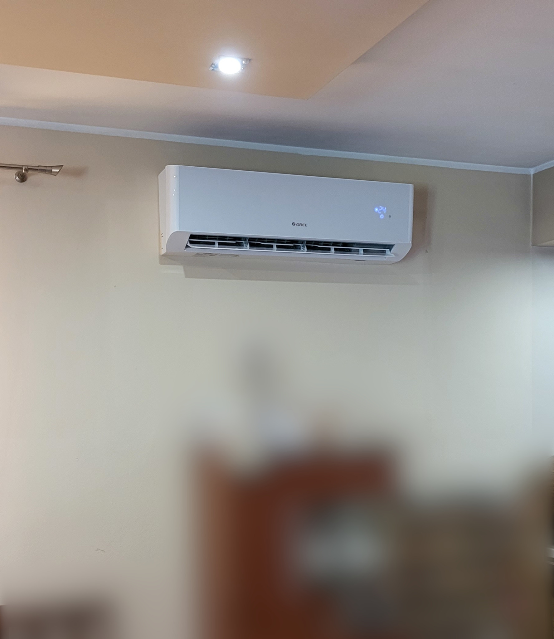 Biała klimatyzacja marki Gree zamontowana na ścianie w jasnym pomieszczeniu, z widocznym wyświetlaczem temperatury.