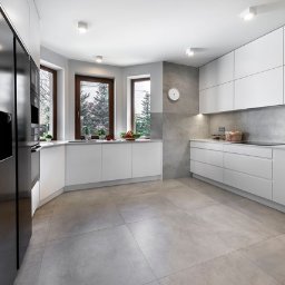 Wasze Wnętrze - Nowoczesna, jasna kuchnia z białymi szafkami bez uchwytów i czarną lodówką. Okno z widokiem na zieleń. Minimalistyczny design z szarym blatem i płytkami.