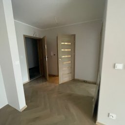 Paweł Kaczówka CONSULTING - Wnętrze pokoju po remoncie z parkietem ułożonym w jodełkę, świeżo pomalowanymi ścianami i dwiema otwartymi drewnianymi drzwiami.