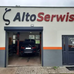 Warsztat samochodowy z podnośnikiem, widoczny samochód BMW 320i z otwartą maską, szyld Alto Serwis nad wjazdem, biuro z godzinami otwarcia po prawej stronie.