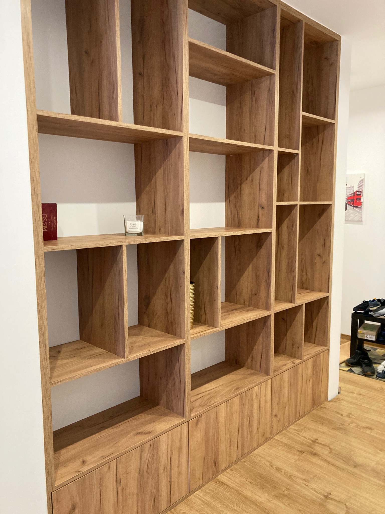 Regał z drewnopodobnej płyty z otwartymi półkami i szafkami na dole, w minimalistycznym wnętrzu z obrazem londyńskiego autobusu w tle.