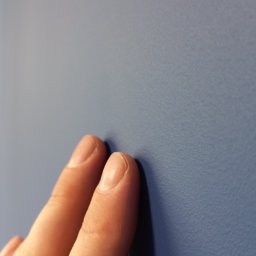 Stachu ReMake - Dwa palce dotykają świeżo pomalowanej, gładkiej ściany w odcieniu niebieskiego, ukazując jej fakturę.