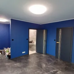 Wnętrze pomalowane na niebiesko we Wrocławiu, z widocznymi drzwiami z dekoracyjnymi paskami i fragmentem łazienki w tle, ukazujące efekt końcowy prac.