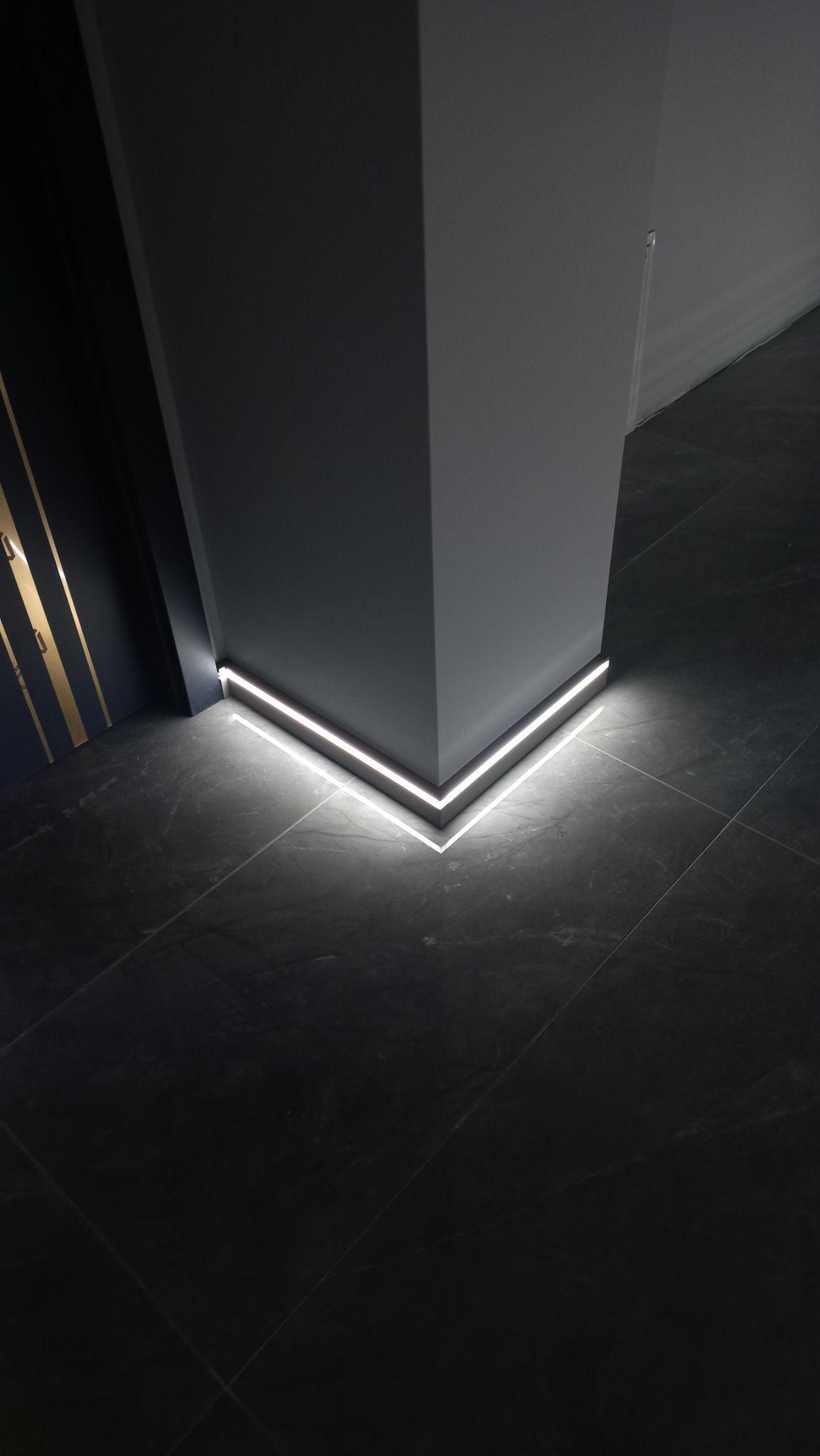 Szary filar z oświetleniem LED przypodłogowym na czarnej, błyszczącej posadzce, widok z dołu.