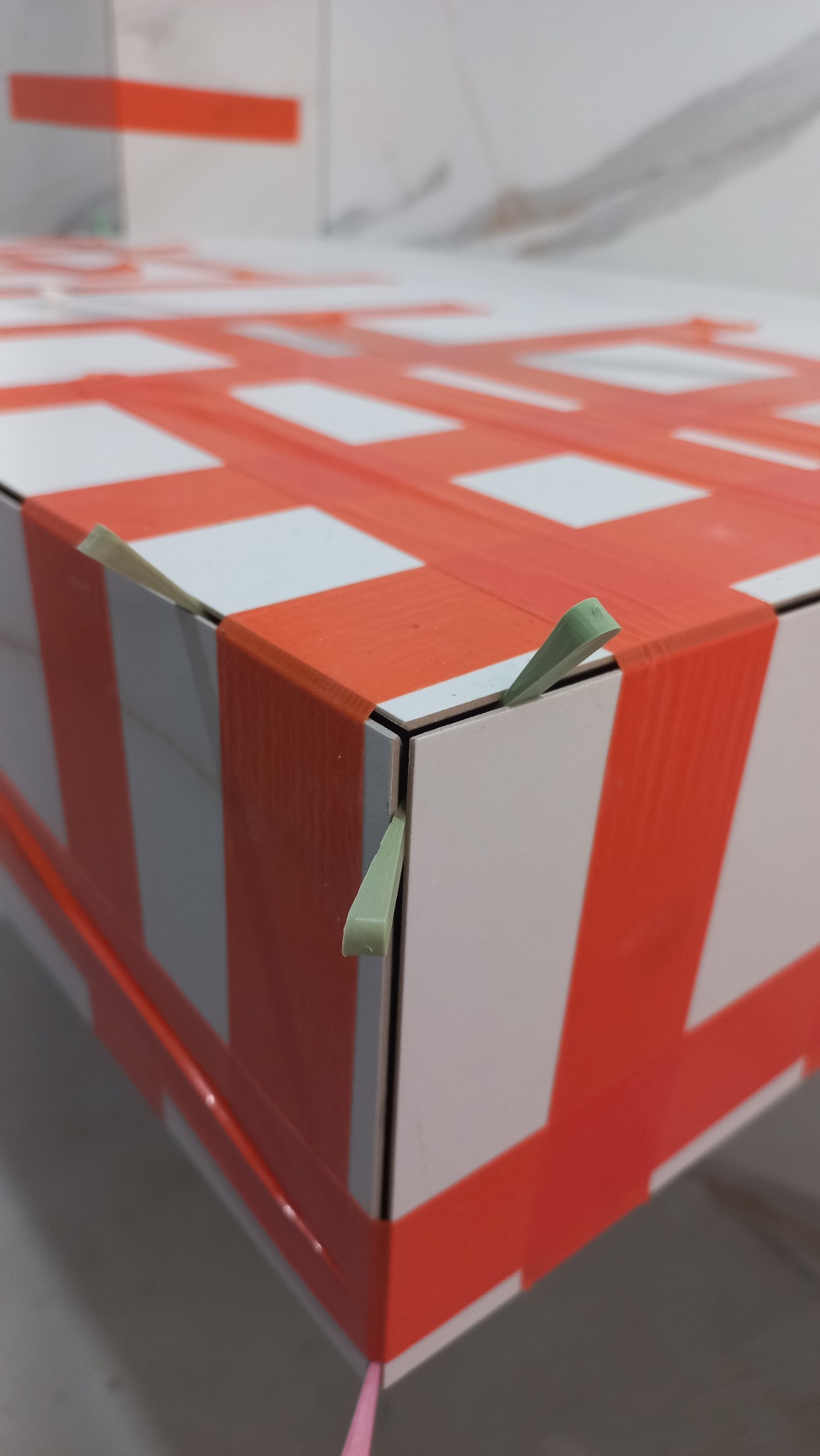 Detal płytek ceramicznych układanych z użyciem krzyżyków dystansowych, tworzących wzór czerwono-białej kraty, widok z bliska na narożnik.