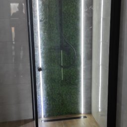 Kompleksowe wykończenia wnętrz - Nowoczesna kabina prysznicowa z czarnymi profilami, podświetlona listwami LED, z zielonym panelem dekoracyjnym imitującym mech na ścianie, oraz odpływem liniowym w podłodze wyłożonej płytkami...