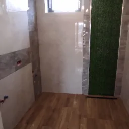 Wykończona łazienka z drewnopodobną podłogą, beżowymi płytkami ściennymi i panelem z mchu na ścianie, widoczne przyłącza wodne