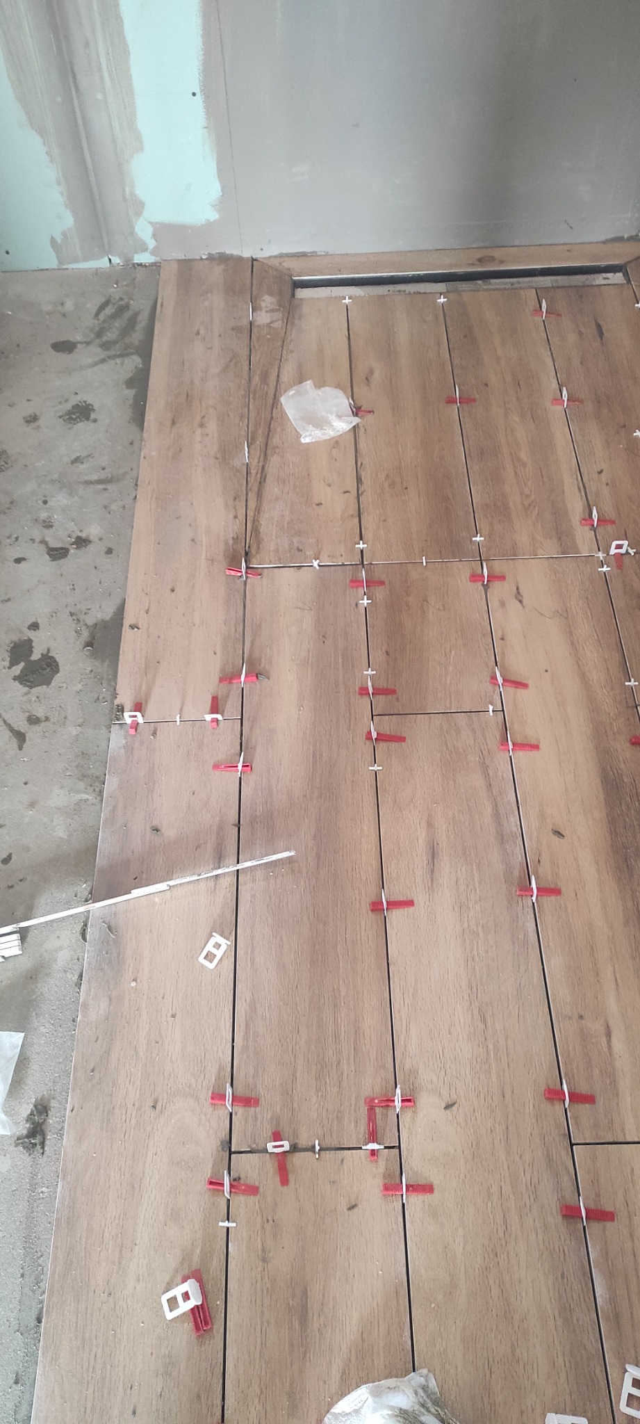 Układanie płytek imitujących drewno z użyciem poziomowania, widoczne krzyżyki i kliny, surowy stan ścian w tle.