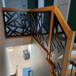 Nowoczesna balustrada z drewna i czarnego metalu o geometrycznym wzorze, widok z góry na schody z oświetleniem LED, w tle jasna podłoga i piec.