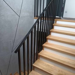 FIRMA MONTERSKO-USŁUGOWA IRO-TECH - Nowoczesne schody z drewnianymi stopniami i czarną metalową balustradą, minimalistyczny design ściany z geometrycznymi liniami.