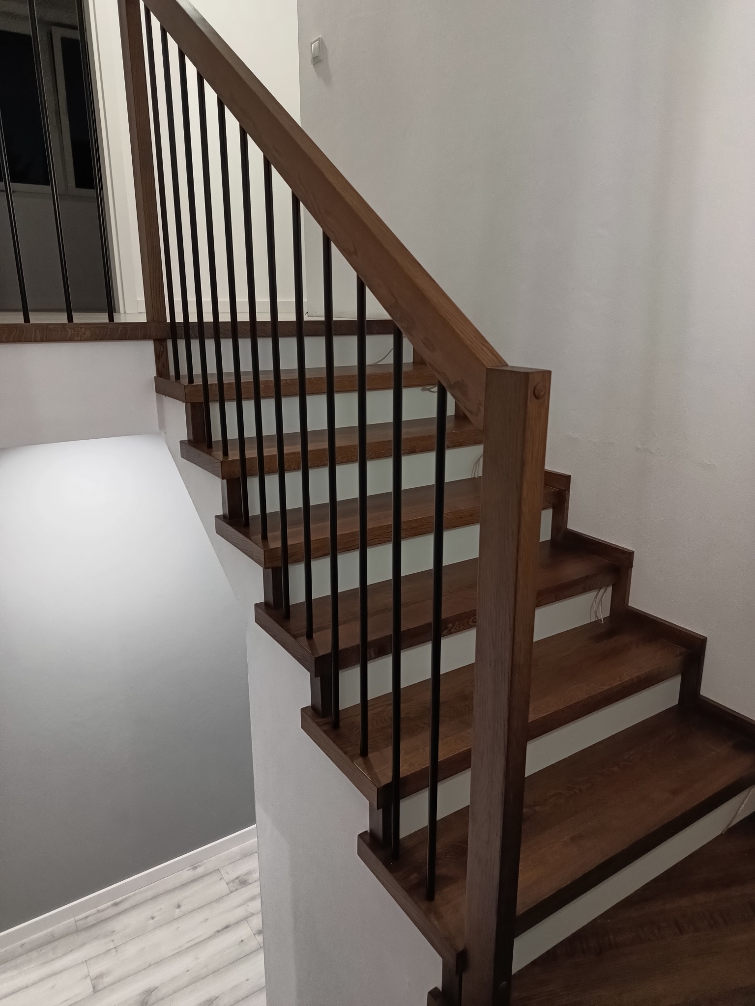 Nowoczesne schody z ciemnego drewna z czarnymi metalowymi balustradami, widok z dołu, minimalistyczny design.