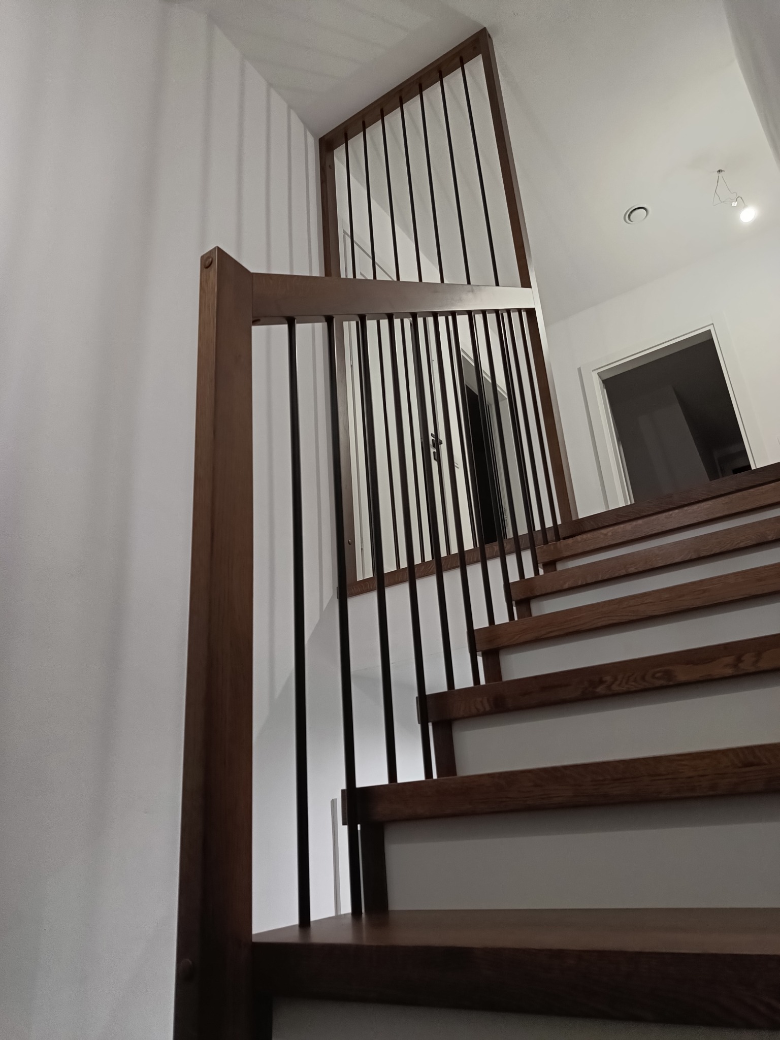 Nowoczesne schody z drewnianymi stopniami i balustradą z czarnymi, pionowymi prętami, widok z dołu, minimalistyczny design.