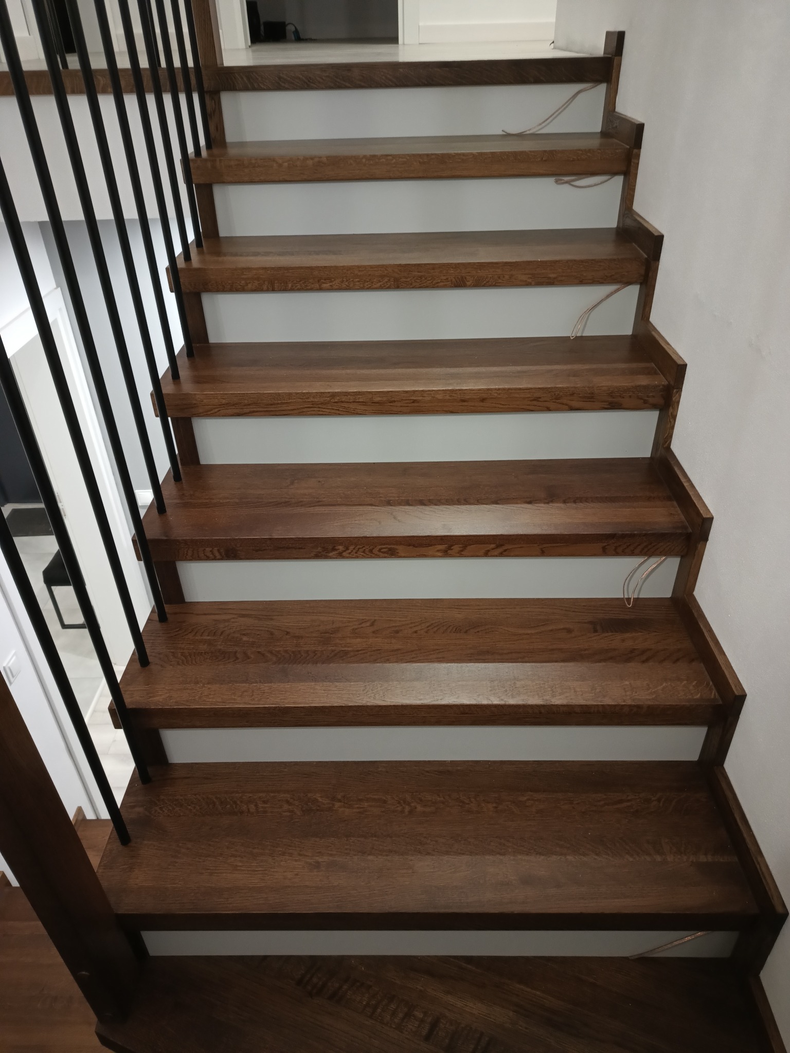 Nowoczesne schody z ciemnego drewna z czarną, minimalistyczną balustradą, widok z góry na stopnie i białe podstopnice.