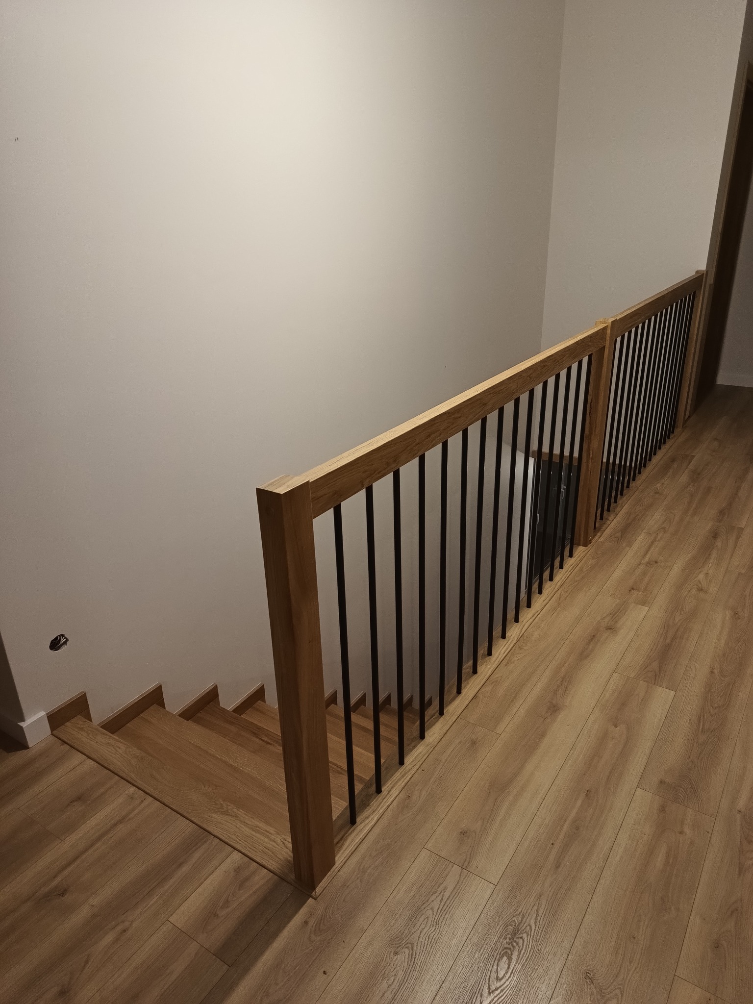 Jasne, drewniane schody z czarnymi, metalowymi prętami balustrady w domu w Iwierzycach, widok z góry.