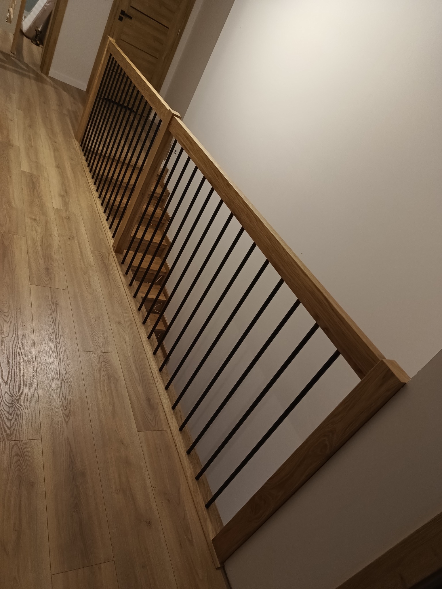 Nowoczesne schody z drewnianymi stopniami i balustradą z drewnianą ramą i czarnymi, metalowymi prętami, widok z góry na dół, dopasowana drewniana podłoga.