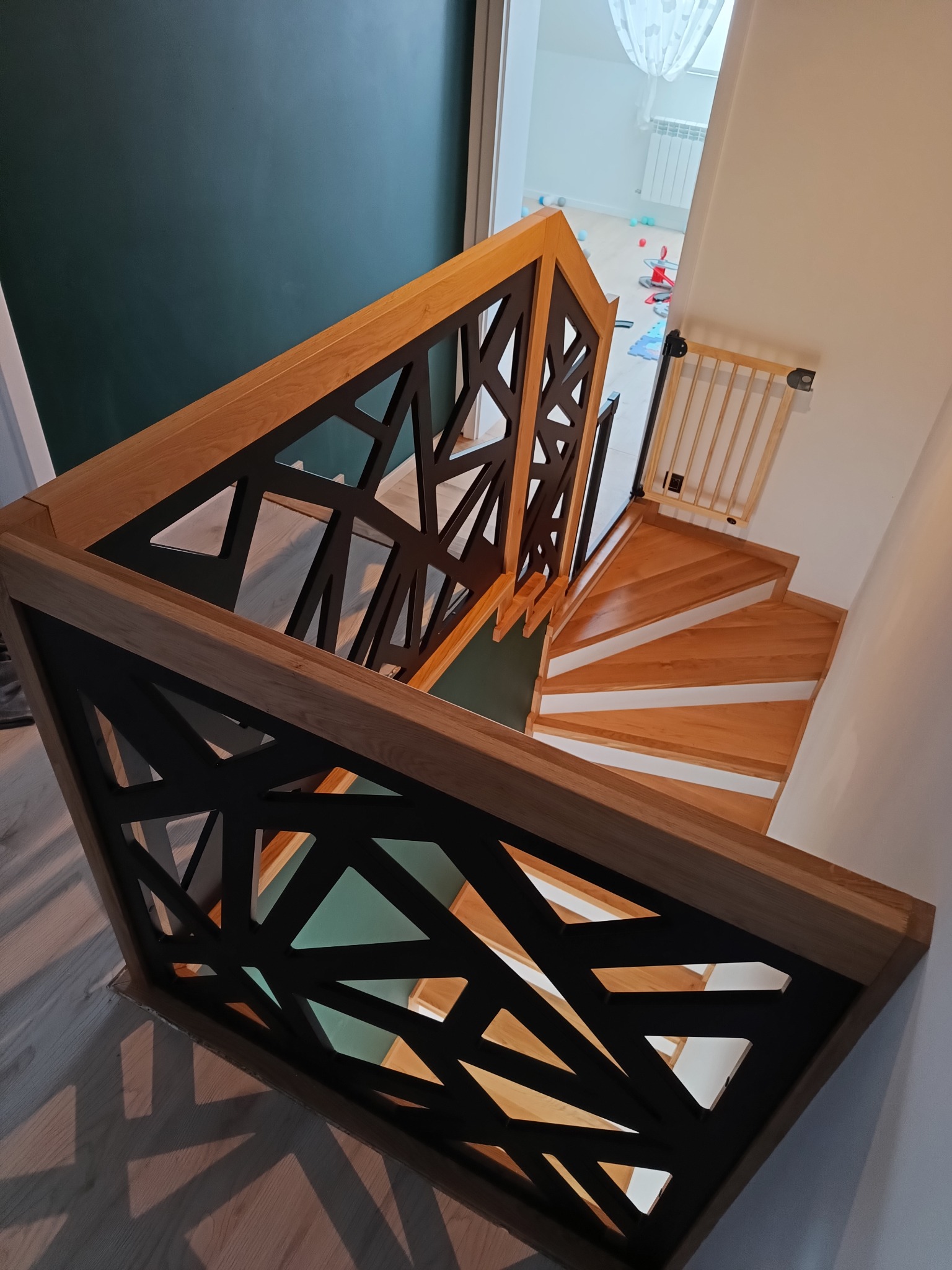 Nowoczesne schody z drewnianymi stopniami i ażurową balustradą z geometrycznym wzorem w kolorze czarnym, widok z góry.